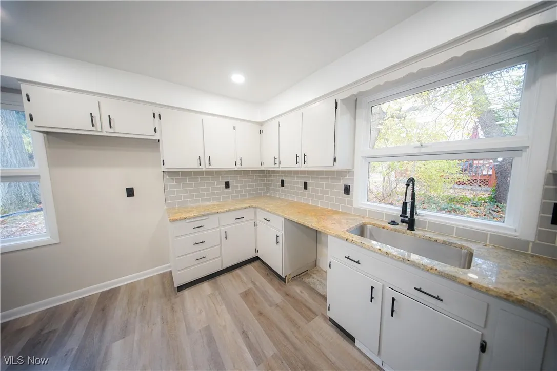 Kitchen featuring white cabinetry, light stone counters, light wood-type flooring, tasteful backsplash, and recessed lighting