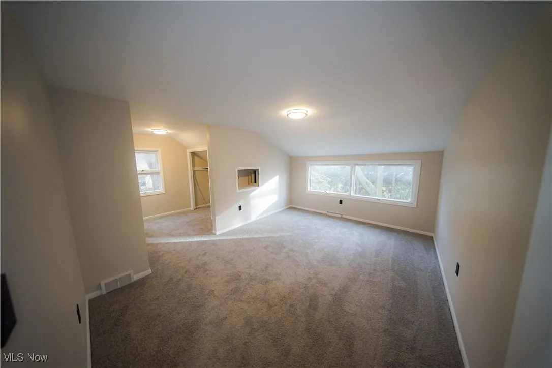 Additional living space with carpet, vaulted ceiling, and a wall unit AC