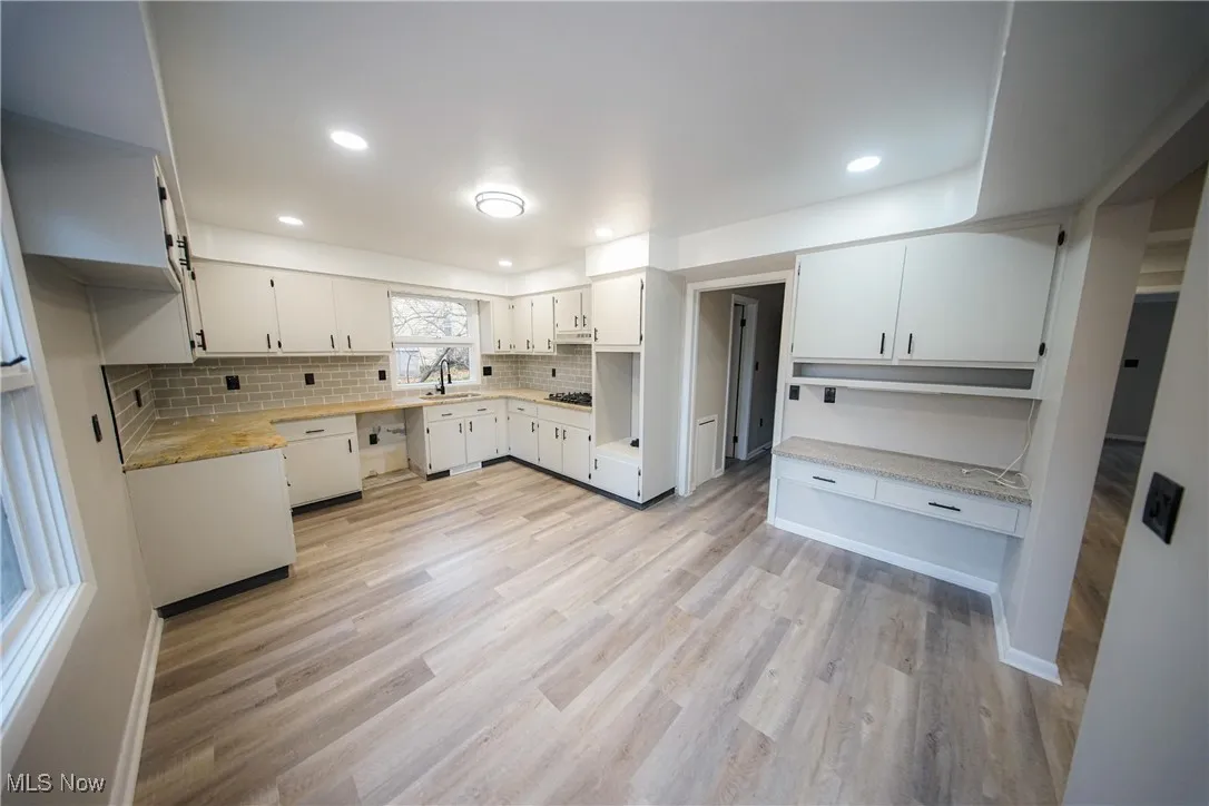 Kitchen with white cabinets, tasteful backsplash, light wood-type flooring, light stone countertops, and open shelves