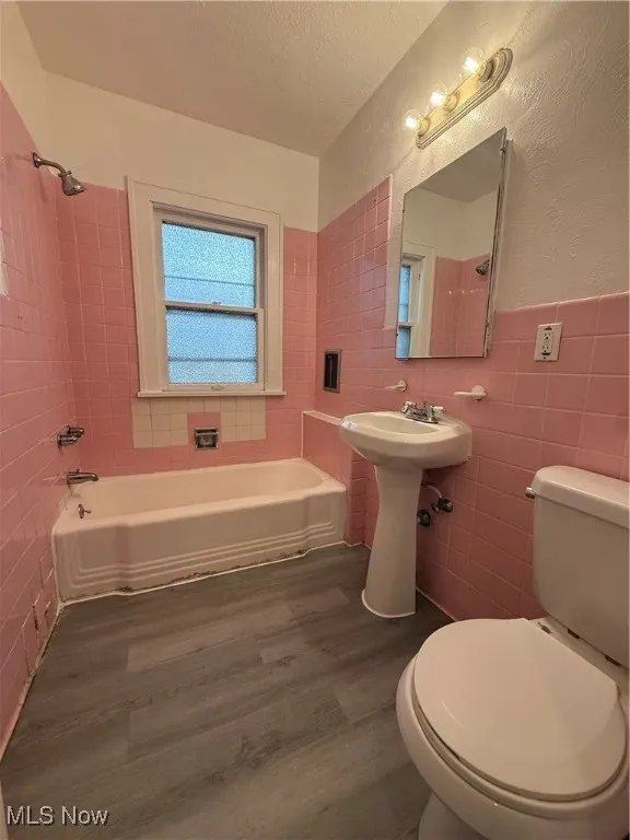 Full bath featuring shower / washtub combination, a textured ceiling, dark wood-style floors, tile walls, and a textured wall