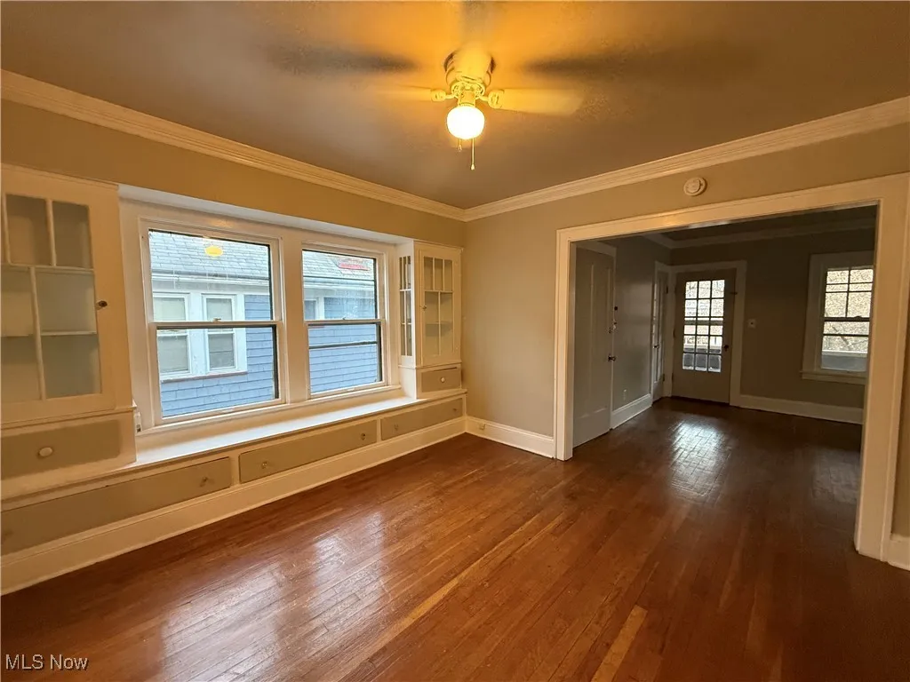 Unfurnished room with dark wood finished floors, crown molding, and a ceiling fan