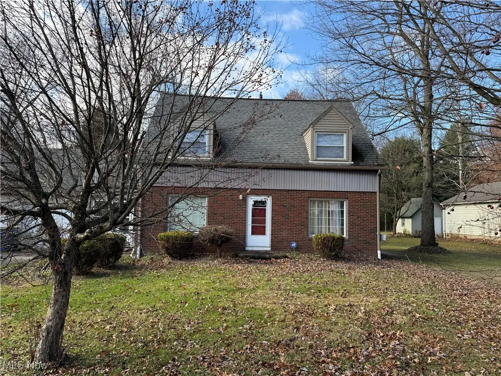 Duplex featuring brick siding, a front lawn, and roof with shingles