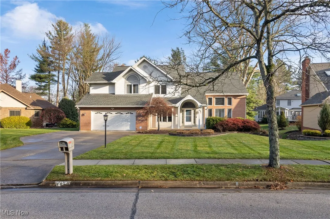 Traditional-style home featuring brick siding, driveway, a front lawn, and a garage
