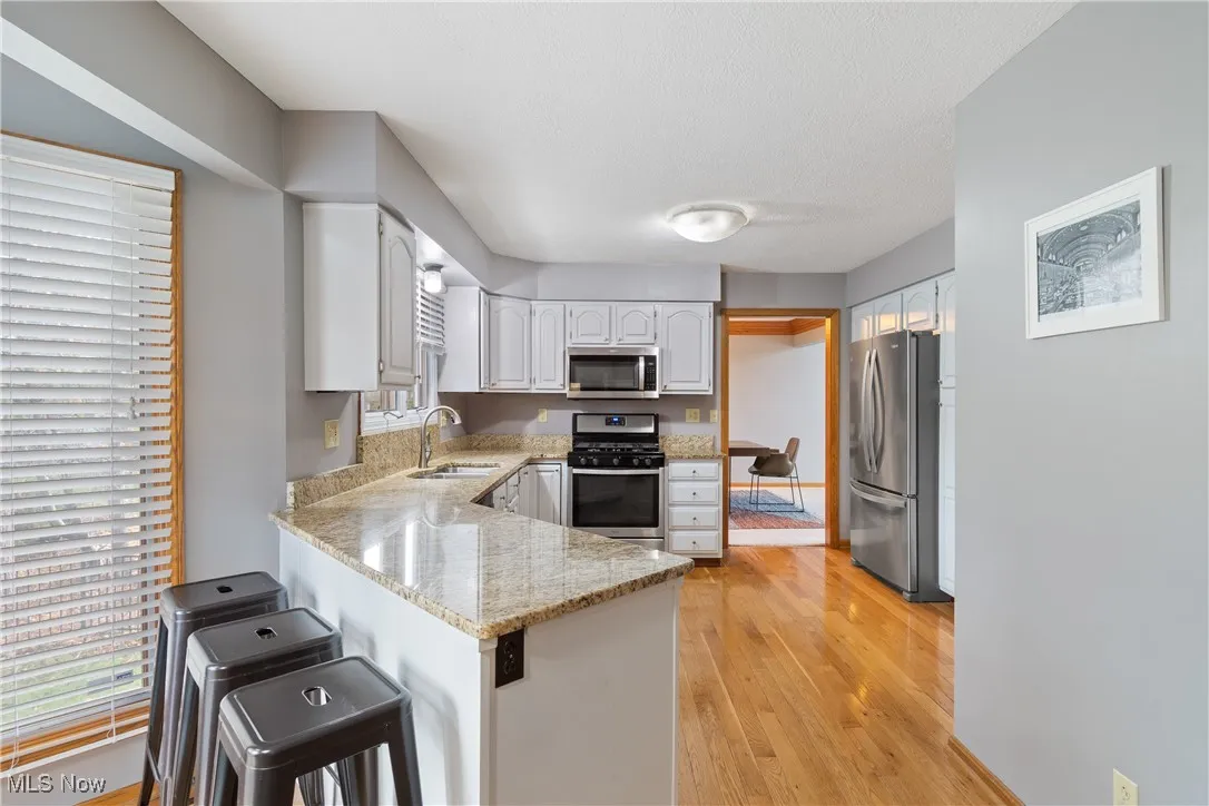 Kitchen with stainless steel appliances, white cabinetry, light stone countertops, a peninsula, and light wood-style floors