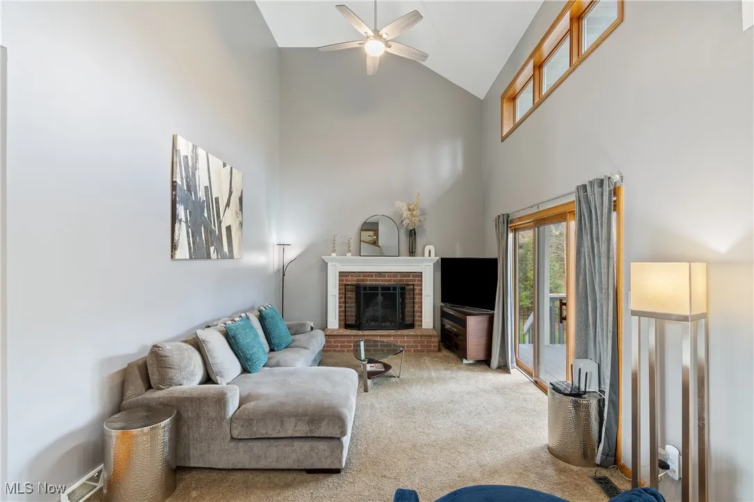 Carpeted living room featuring a fireplace, high vaulted ceiling, and ceiling fan