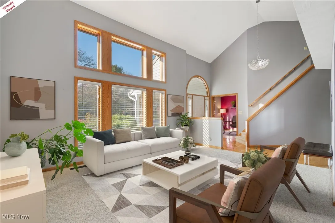 Living room with high vaulted ceiling, stairs, and carpet flooring