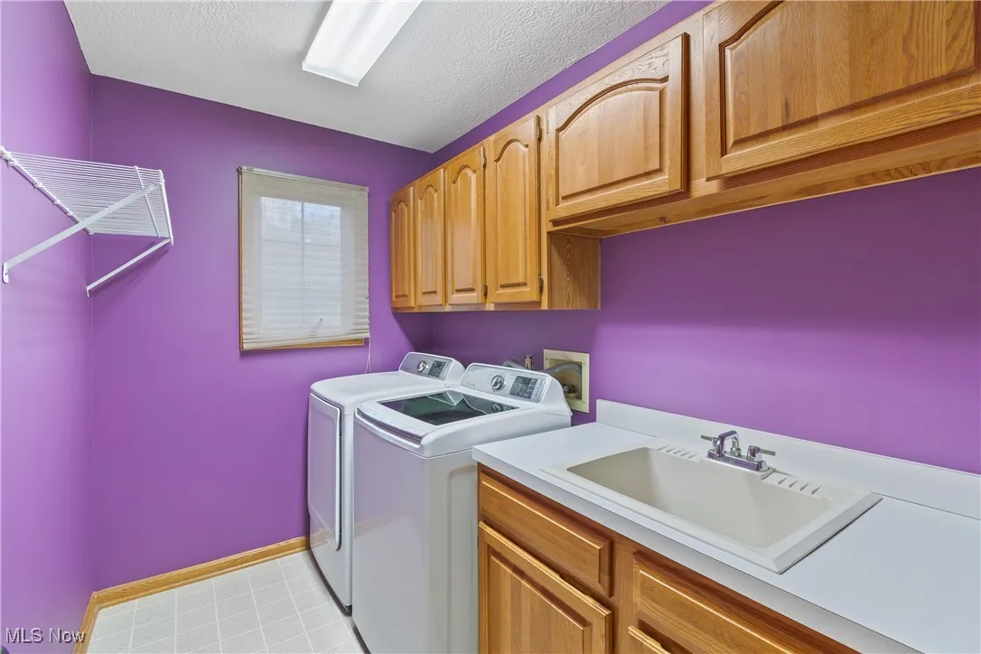 Laundry area featuring a textured ceiling, washer and clothes dryer, cabinet space, and light flooring