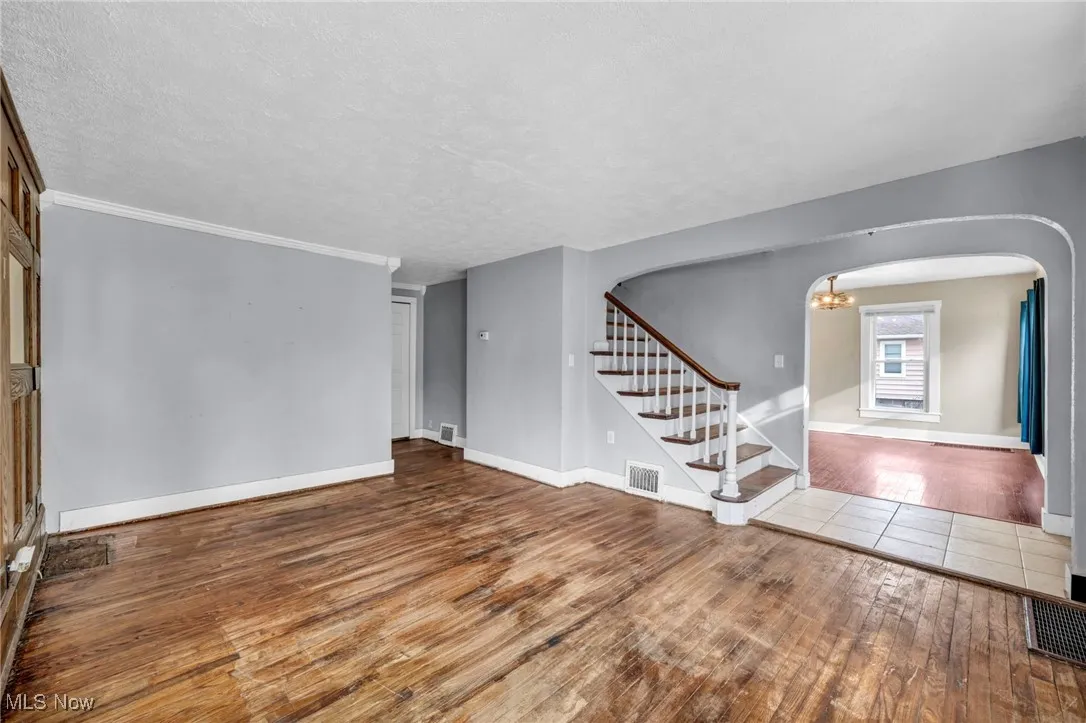 Unfurnished living room featuring a chandelier, stairway, a textured ceiling, hardwood / wood-style flooring, and arched walkways