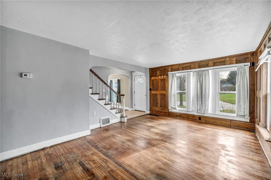 Unfurnished living room with arched walkways, hardwood / wood-style floors, a textured ceiling, and stairs