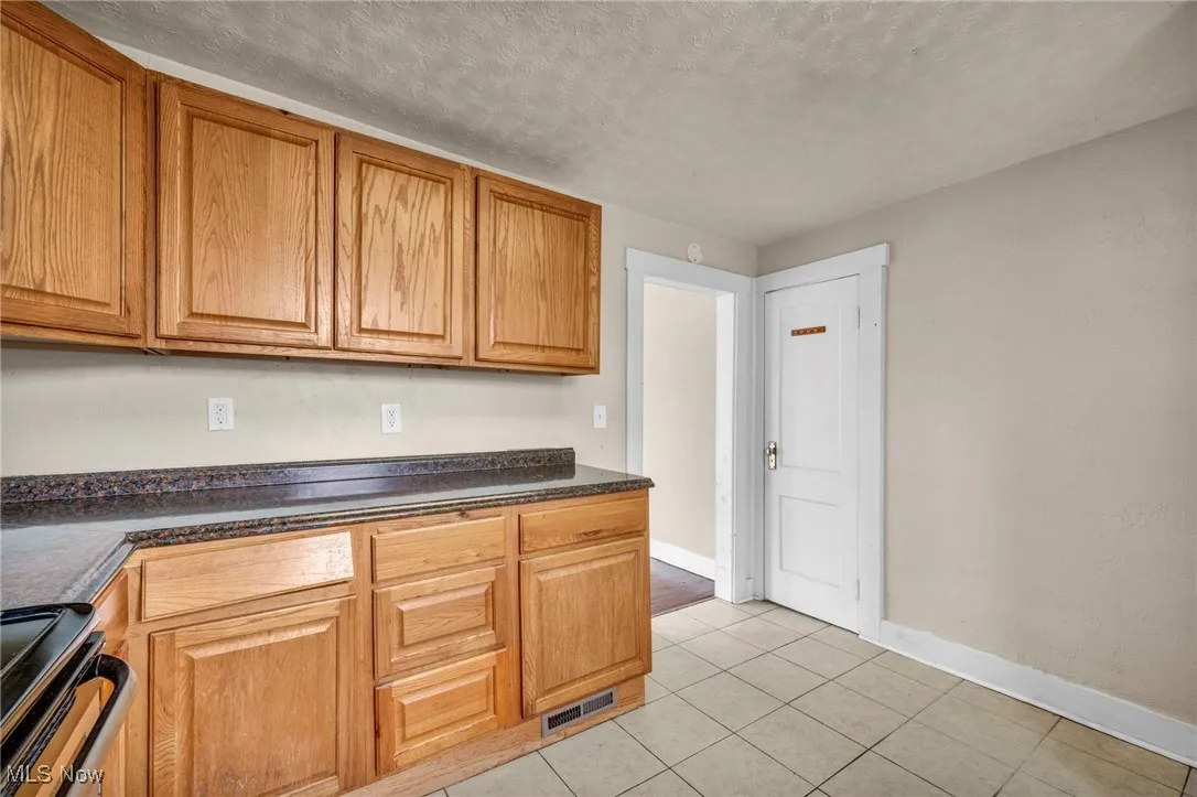 Kitchen featuring black range oven, dark countertops, a textured ceiling, light tile patterned floors, and brown cabinetry
