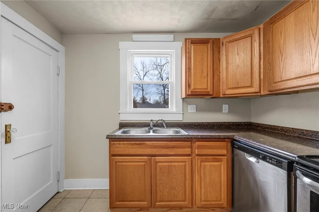Kitchen with dishwasher, light tile patterned flooring, dark countertops, and brown cabinetry