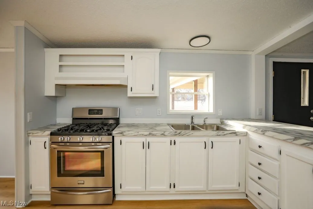 Kitchen with gas stove, white cabinets, open shelves, light countertops, and a textured ceiling