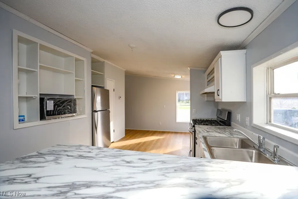 Kitchen with open shelves, appliances with stainless steel finishes, white cabinetry, crown molding, and a textured ceiling