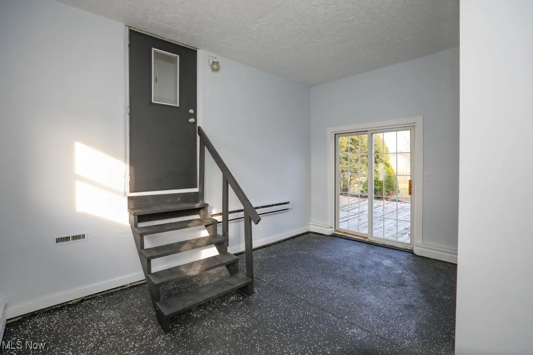 Stairway featuring a textured ceiling and a baseboard radiator