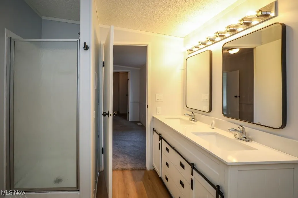 Full bath featuring a textured ceiling, double vanity, a stall shower, vaulted ceiling, and light wood-type flooring