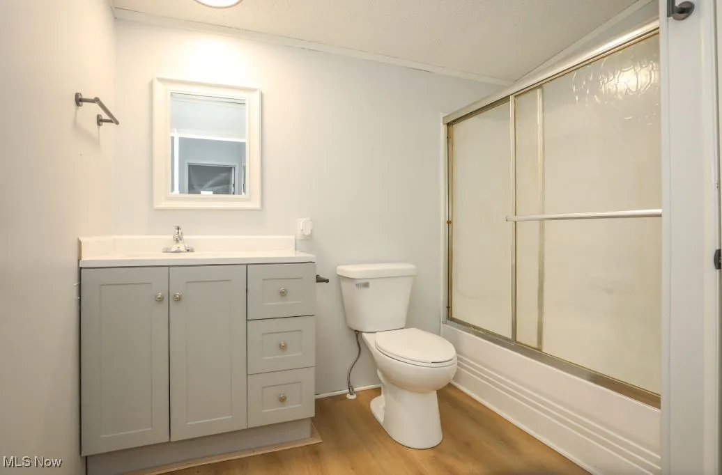 Full bath with vanity, enclosed tub / shower combo, and light wood-style floors