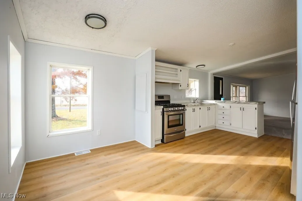 Kitchen featuring gas stove, white cabinets, light countertops, a textured ceiling, and a peninsula