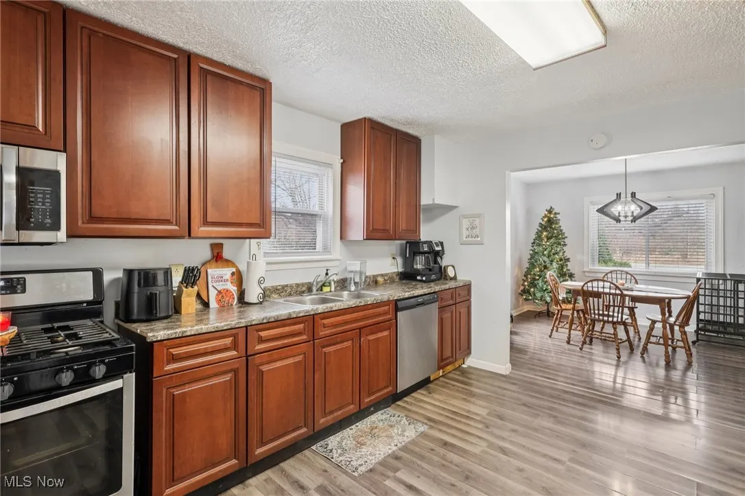 Kitchen with stainless steel appliances, decorative light fixtures, a textured ceiling, light wood-type flooring, and brown cabinets