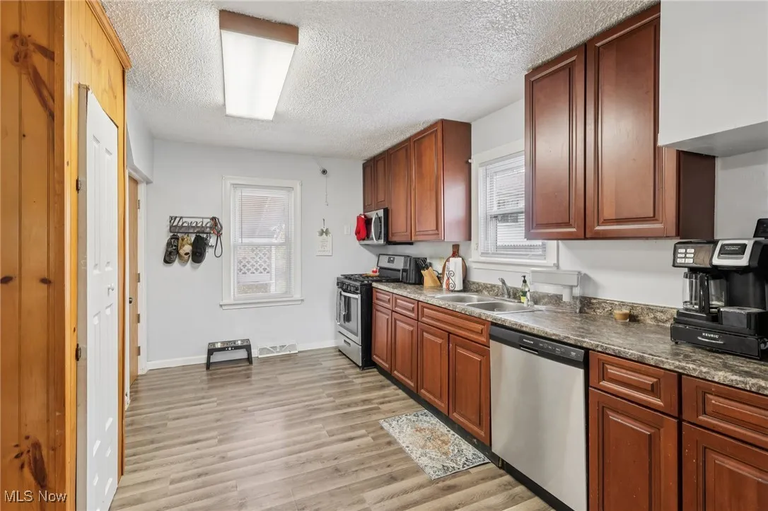 Kitchen with appliances with stainless steel finishes, light wood-style flooring, a textured ceiling, dark countertops, and brown cabinets