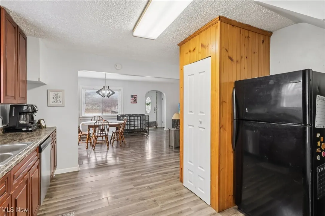 Kitchen with freestanding refrigerator, decorative light fixtures, dark countertops, light wood-style floors, and a textured ceiling