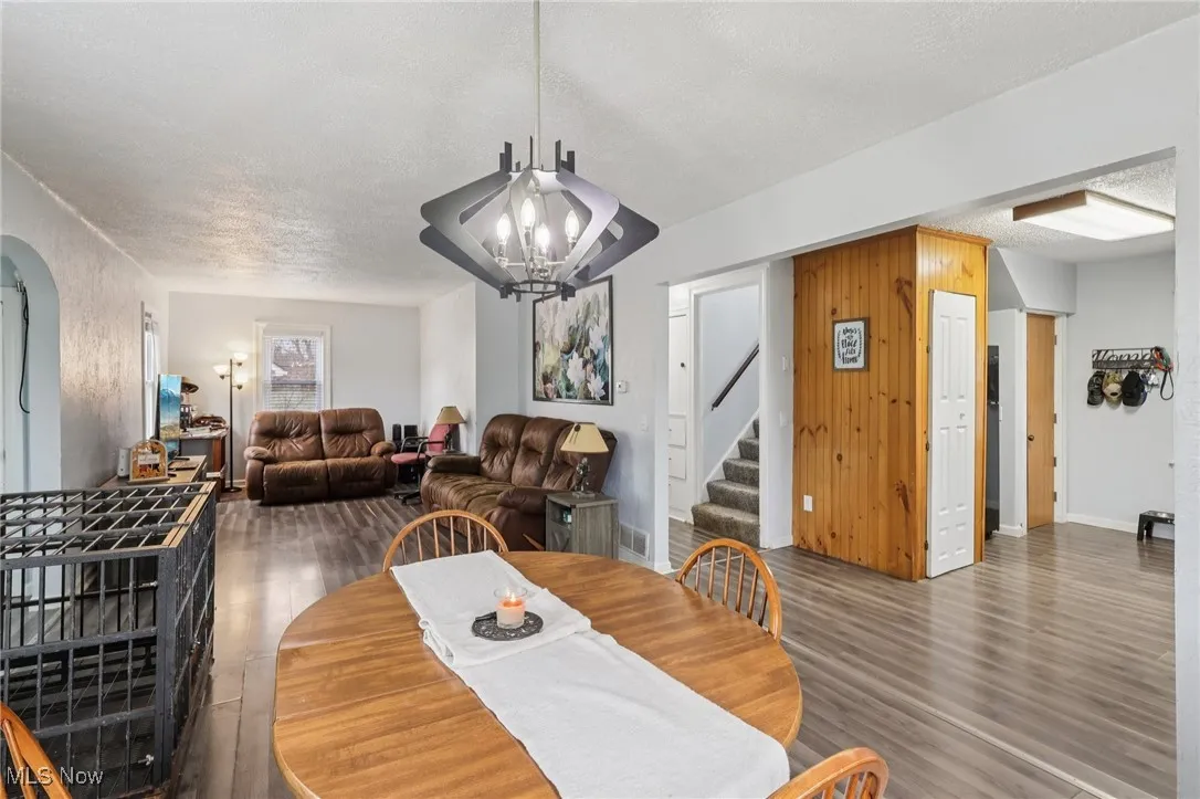 Dining area with stairway, a textured ceiling, dark wood-style flooring, arched walkways, and a chandelier