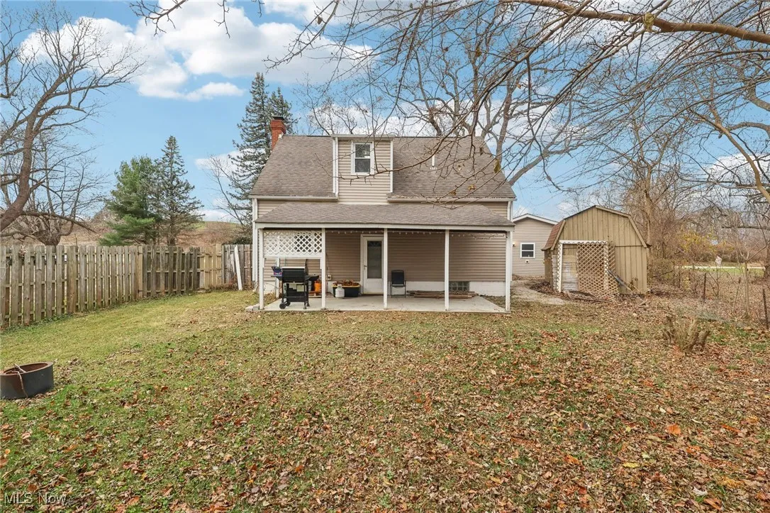 Back of property featuring a chimney, a patio, a storage unit, a fenced backyard, and roof with shingles