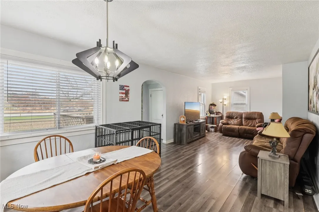Dining room with arched walkways, wood finished floors, a textured ceiling, and a chandelier