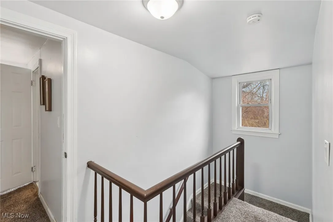 Corridor with dark carpet, an upstairs landing, and lofted ceiling