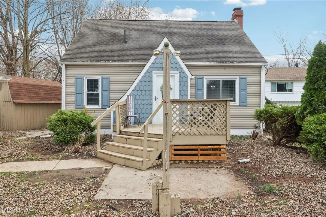 Back of property with a deck, roof with shingles, a chimney, and an outdoor structure
