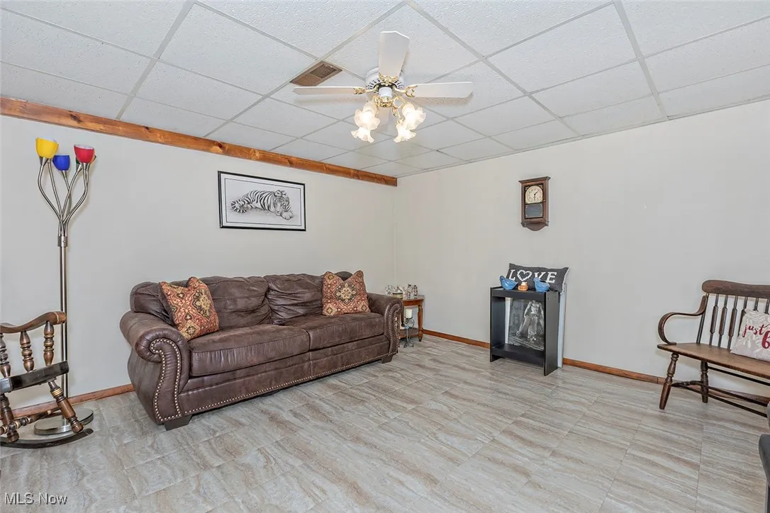 Living area with ceiling fan, a paneled ceiling, and light floors