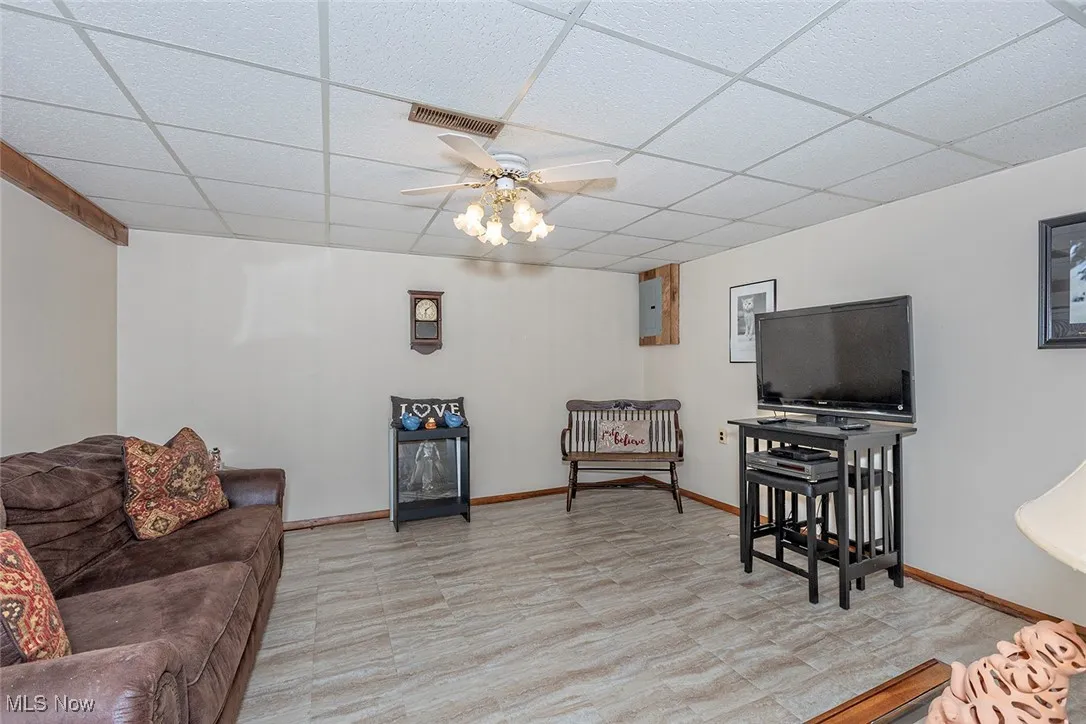 Living room with a ceiling fan, a drop ceiling, and light floors