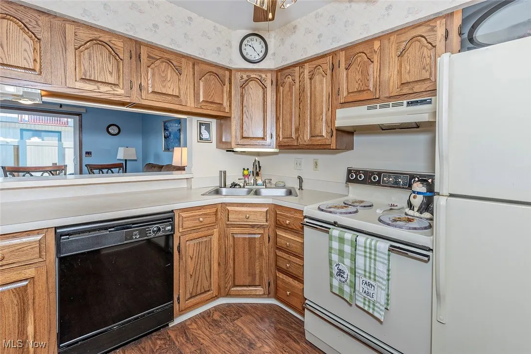 Kitchen with white appliances, brown cabinetry, light countertops, under cabinet range hood, and dark wood-type flooring
