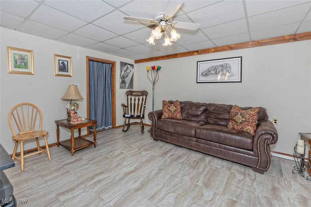 Living area featuring a ceiling fan, a drop ceiling, and tile patterned floors