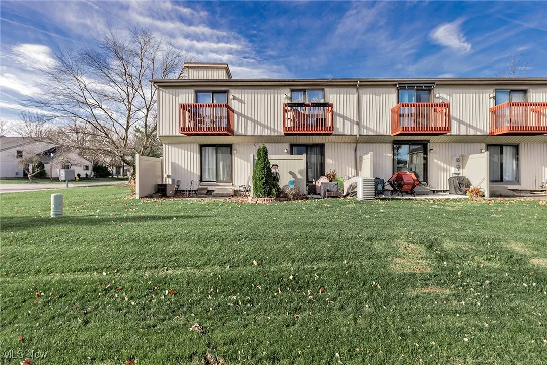 Back of house with a balcony, a patio, and a lawn