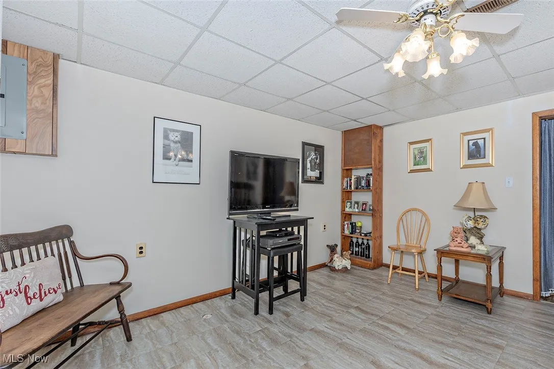 Living area featuring a drop ceiling, electric panel, ceiling fan, and light flooring