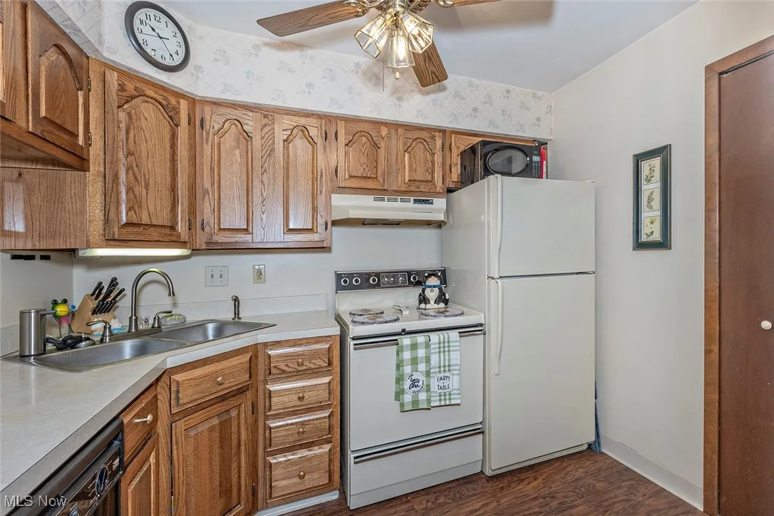 Kitchen with white appliances, brown cabinets, light countertops, and under cabinet range hood