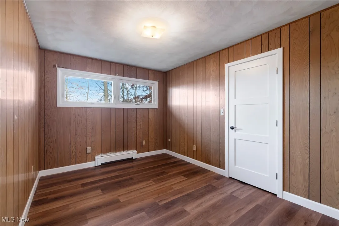 Empty room featuring wooden walls, a baseboard radiator, and dark wood finished floors