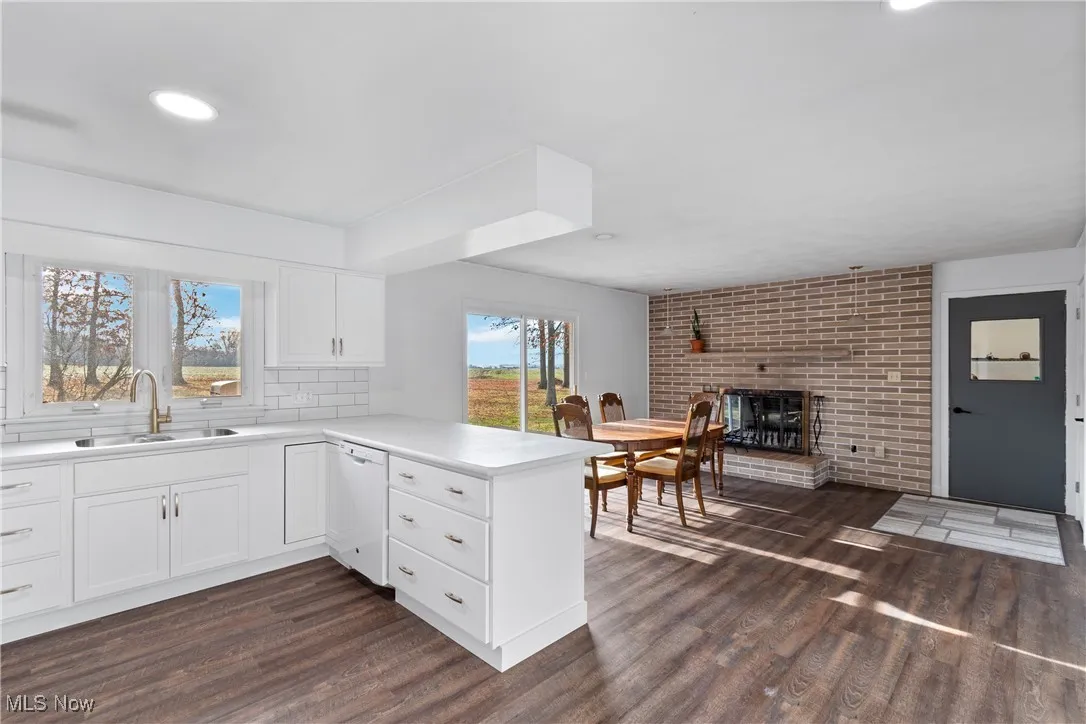 Kitchen featuring a peninsula, white cabinets, light countertops, dark wood finished floors, and a fireplace