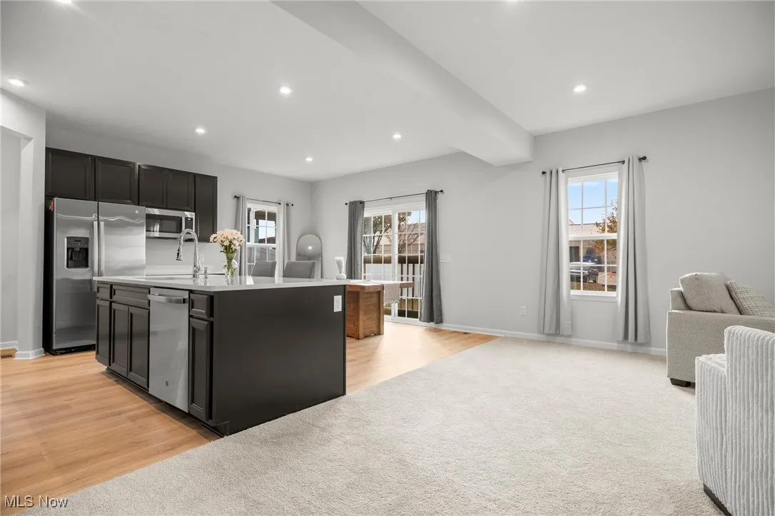 Kitchen featuring open floor plan, a center island with sink, stainless steel appliances, dark cabinets, and recessed lighting