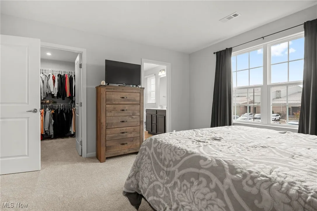 Bedroom with a spacious closet, light colored carpet, and ensuite bath