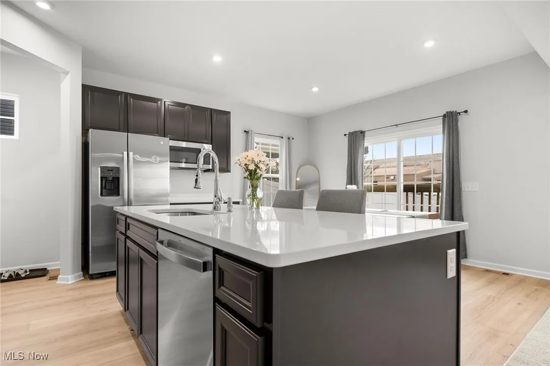 Kitchen with stainless steel appliances, a kitchen island with sink, light wood finished floors, light stone counters, and recessed lighting