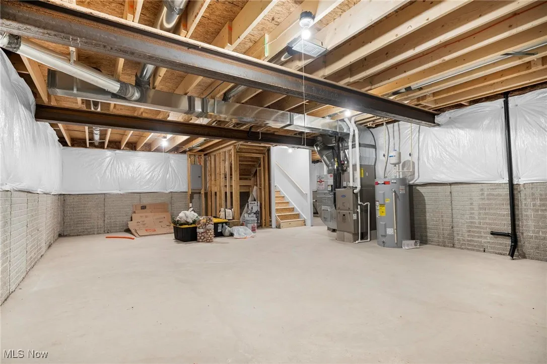 Unfinished basement with brick wall, water heater, stairs, heating unit, and electric panel
