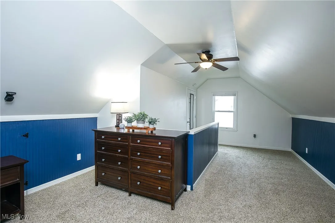 Additional living space with light colored carpet, lofted ceiling, wood walls, and a ceiling fan