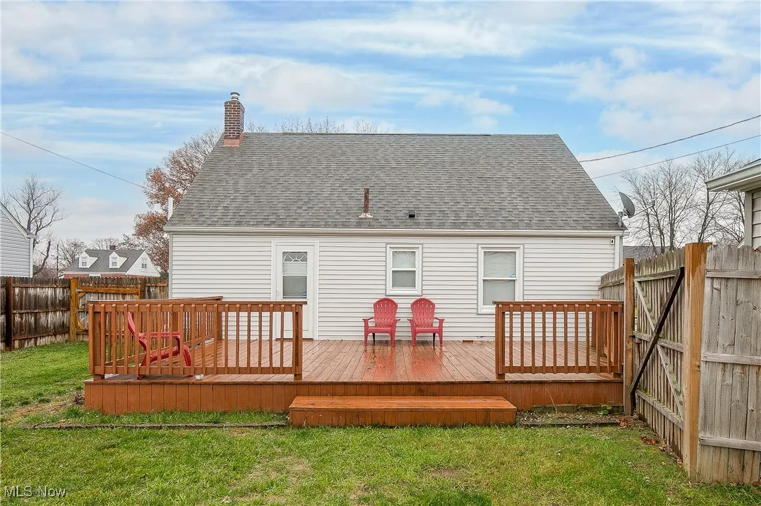 Rear view of property featuring a fenced backyard, a wooden deck, roof with shingles, and a chimney