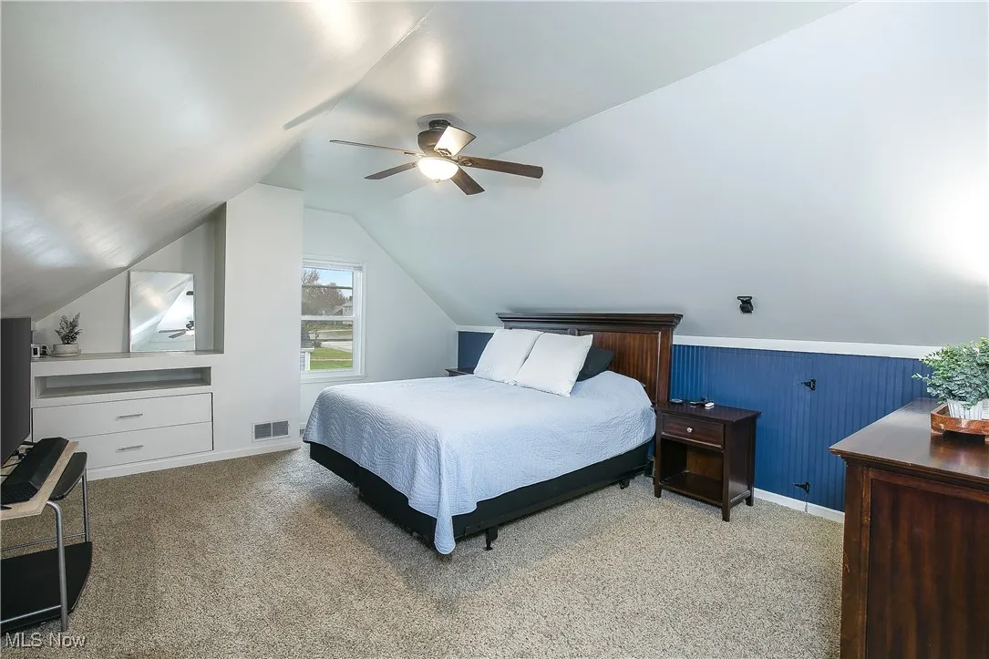 Bedroom with light carpet, a ceiling fan, lofted ceiling, and wainscoting