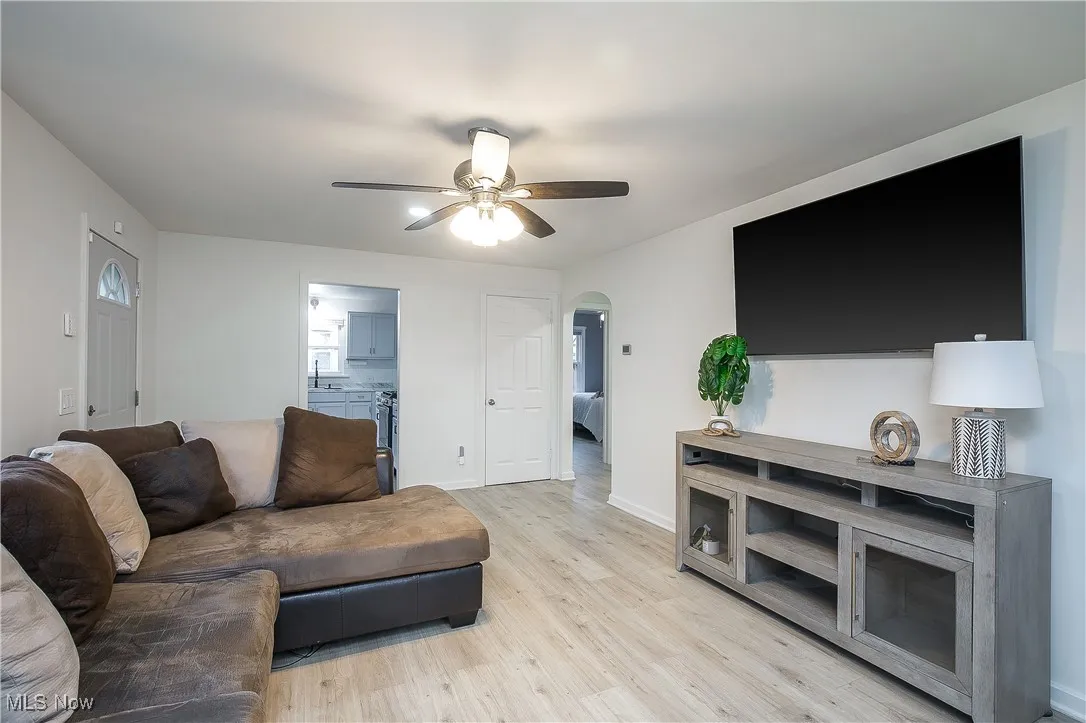 Living area with arched walkways, light wood-style floors, and ceiling fan