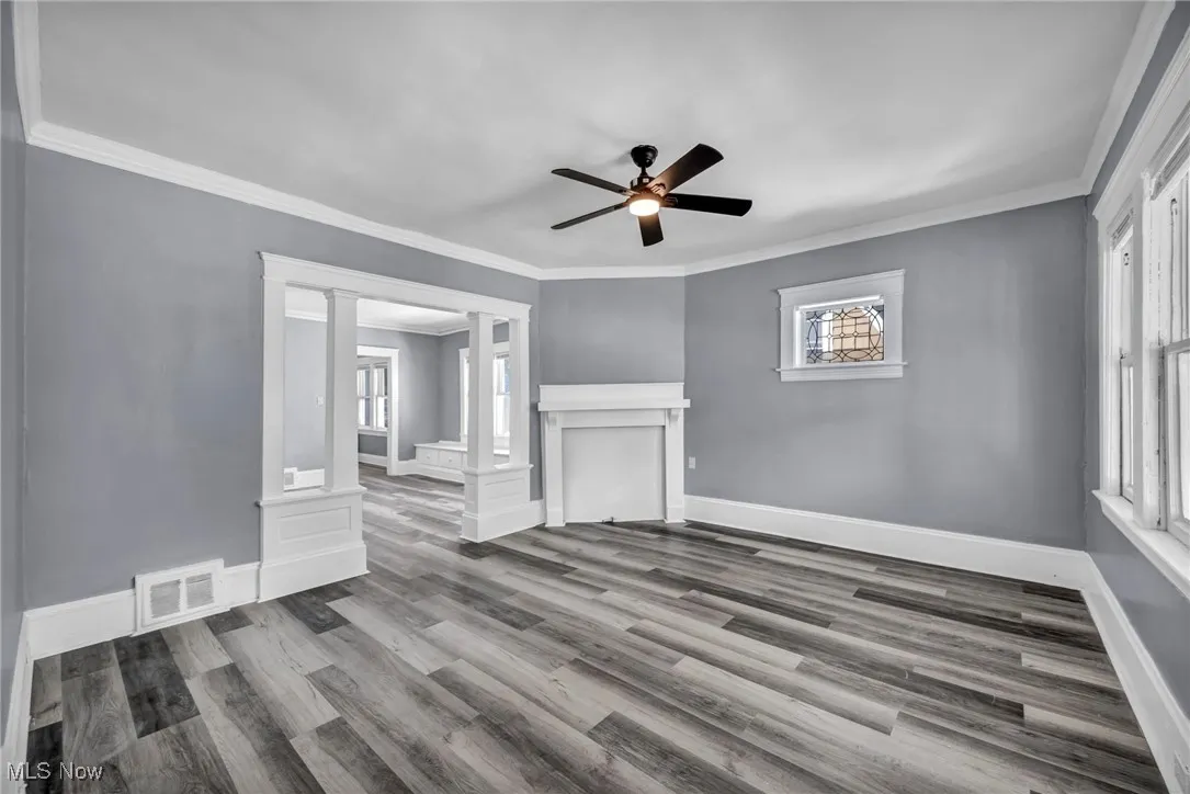 Unfurnished living room with ornamental molding, healthy amount of natural light, wood finished floors, ceiling fan, and decorative columns