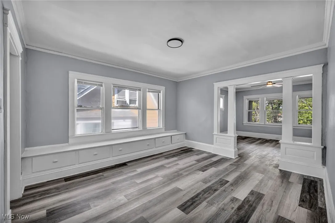 Empty room featuring ornamental molding, a ceiling fan, light wood-style floors, and decorative columns