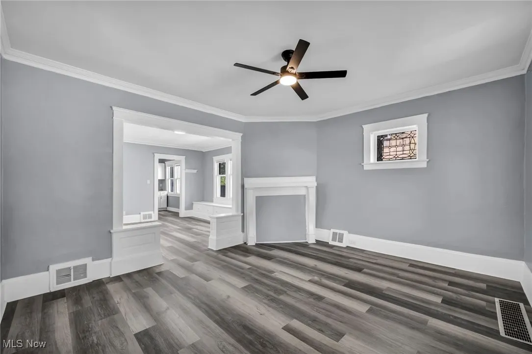 Unfurnished living room with ornamental molding, dark wood-style flooring, plenty of natural light, and a ceiling fan