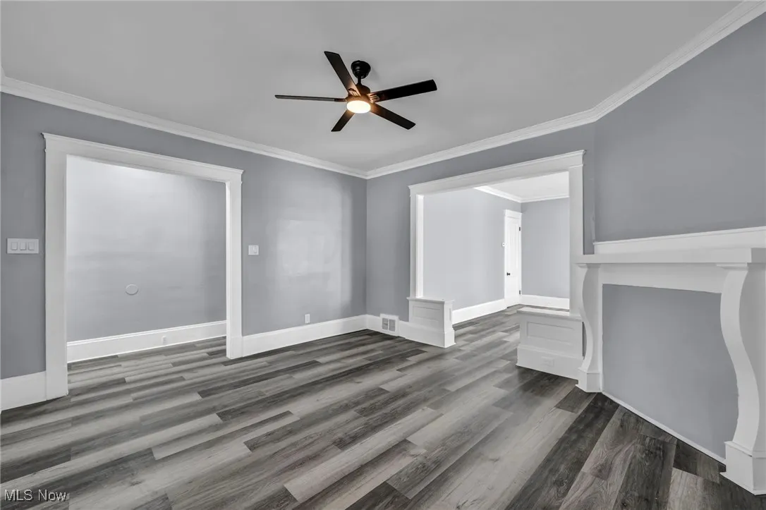 Unfurnished living room featuring ornamental molding, dark wood finished floors, and a ceiling fan